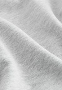 Tissu gris clair avec une texture douce et lisse, présentant un léger éclat et un subtil motif de tricot horizontal. Des plis sont présents.