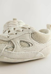 Baskets en suédine beige avec des panneaux en mailles, bout rond et lacets plats. Elles sont dotées d'une semelle texturée et de détails de couture subtils. Design léger.