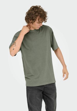 Olivengrøn bomulds t-shirt med rund hals og korte ærmer, der har en afslappet pasform og glat tekstur, båret med mørke jeans.