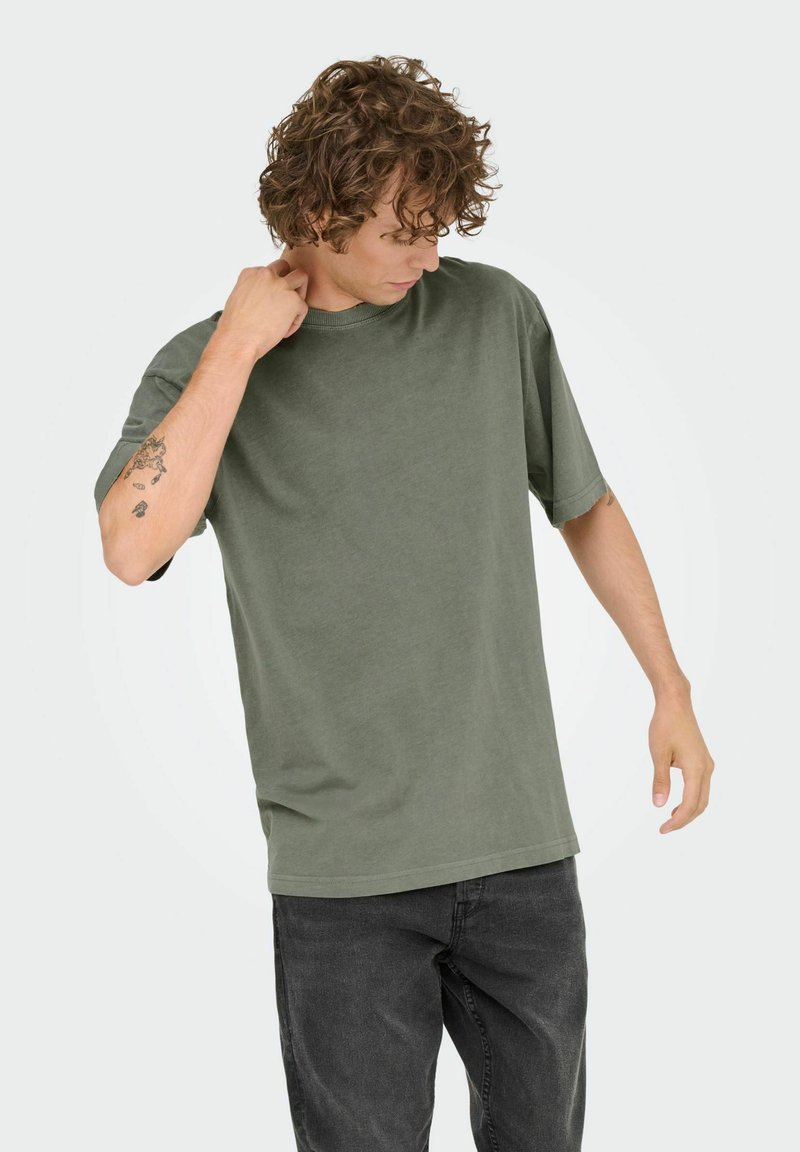 Olivengrøn bomulds t-shirt med rund hals og korte ærmer, der har en afslappet pasform og glat tekstur, båret med mørke jeans.