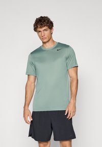 Jasnozielona, krótka koszulka sportowa z materiału odprowadzającego wilgoć, z okrągłym dekoltem i czarnym logo Nike na lewej piersi.