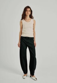 Krämfärgad ribbad linne, löst sittande svarta jeans och vita tofflor med svarta detaljer. Enkel design, mjuka texturer, inga synliga mönster.