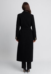 Czarny długi płaszcz wełniany z paskiem w talii, z kołnierzem typu notch i złotymi guzikami na rękawach.