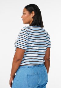 Triibuline puuvillane t-särk, millel on horisontaalsed sinised, valged ja pruunid triibud, lühikesed varrukad ning ümar kaelus, kombineeritud kõrge talje ja siniste teksadega.