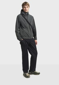 Grå hættejakke med elastiske manchetter, sorte cargo-bukser og grønne vandresko. Outfittet har en sort crossbody-taske og et slankt design.