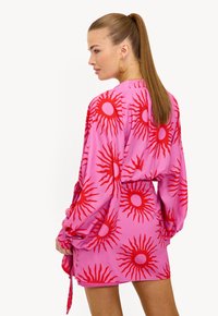 Vestido rosa con estampado de destellos rojos, mangas largas y cintura ceñida. Tela lisa con detalle de lazo en el costado.