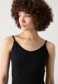 Black camisole with thin straps, v-neck design, made of smooth fabric. Close-fitting and seamless with a simple, minimalistic appearance.