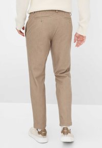 Pantalons à carreaux beiges clairs avec une coupe ajustée, dotés de deux poches arrière et de détails de boutons subtils. Associés à des baskets blanches.