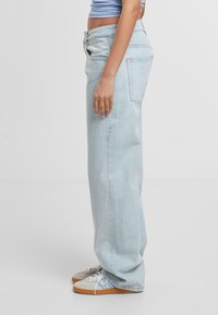 Lichtblauwe denim jeans met een losse pasvorm, hoge taille, rechte pijpen en twee achterzakken. Gecombineerd met grijze sneakers en witte veters.