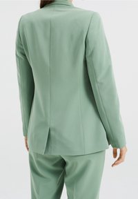 Ljusgrön kavaj med skräddarsydd design, som har en enda slits bak och en mjuk textur, kombinerad med matchande byxor.