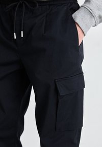 Marine cargo bukser laget av lett stoff, med elastisk liv, sidelommer og en stor sidelomme.