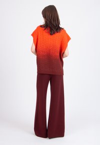 Knitted sweater with a red to brown gradient, featuring short sleeves and a textured pattern, paired with wide-leg brown trousers.