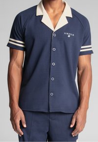 Navy short-sleeve polo shirt with a cream collar, featuring three buttons, white striped accents on sleeves, and front logo. Smooth texture.
