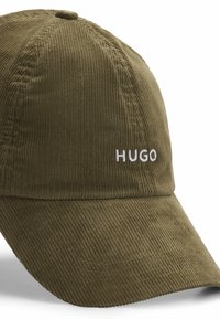 Oliven grøn kordfløjl baseball cap med en buet skygge og broderet "HUGO" logo i hvid på forsiden. Synlig struktureret stofdetalje.