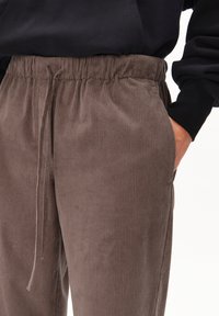 Pantalons en velours côtelé marron avec une taille élastique et un cordon de serrage. Texture côtelée verticale et poches latérales visibles.