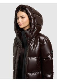 Brun vadderad jacka med glansig yta, oversized huva, tryckknappar och en logotyp på ärmen. Har ett quiltat mönster.