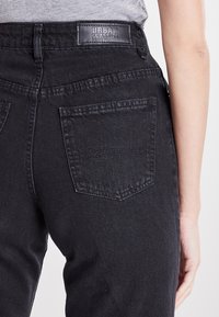 Jeans de mezclilla negra con un diseño clásico de cinco bolsillos. Tejido texturizado con un acabado suave y un parche de cuero con el logo en la cinturilla.