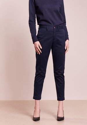 Woman wearing navy pinstripe long-sleeve top, dark navy cropped pants, and black high-heeled shoes standing on beige floor.