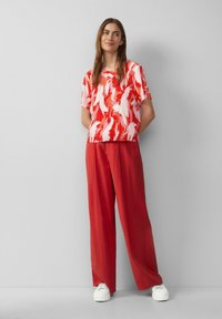 Rood en witte top met korte mouwen en veerpatroon, gecombineerd met rode wijde broek en witte sneakers. Glad materiaal, relaxte pasvorm.