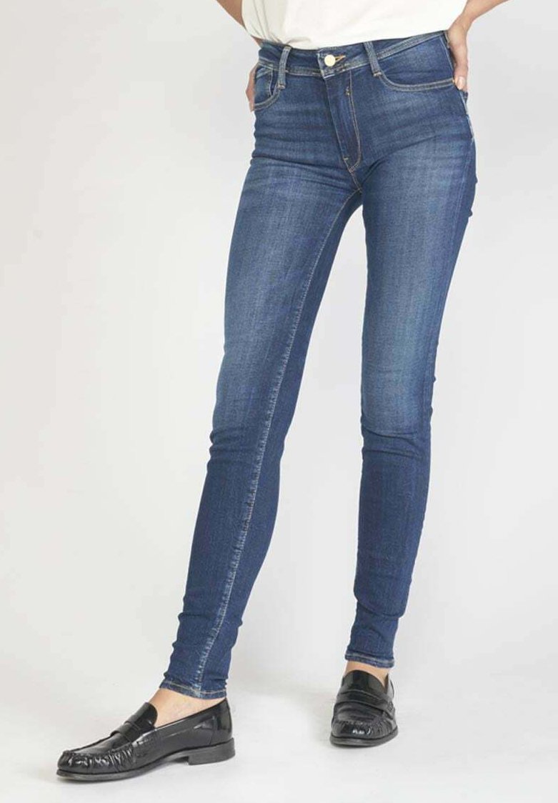 Jeans skinny en denim bleu foncé, avec une taille mi-haute et des accents légèrement décolorés. Associés à des mocassins noirs, mettant en avant un style classique.