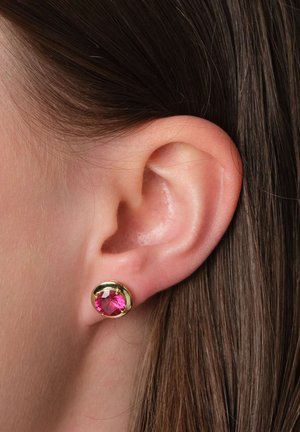 Goldfarbene Ohrstecker mit einem runden rosa Edelstein, der ein glattes Finish und eine klassische Fassung zeigt, die sich vor strukturiertem Hautbild abhebt.