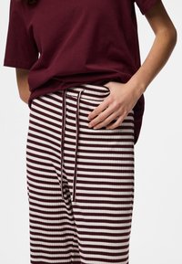 Bordeaux bomuld T-shirt kombineret med cremefarvede og bordeaux stribede bukser med snøre i taljen og tekstureret stof.