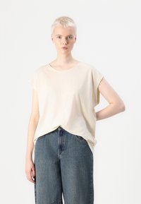 Beige, rövid ujjú felső, laza szabással és kerek nyakkivágással, magas derekú kék farmernadrággal párosítva. Puha textúra, hétköznapi dizájn.