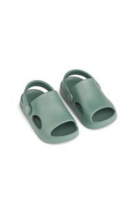 Zöld gumi szandál, nyitott orr-designnal, hátpánttal és vízszintes bordás textúrával a talpbetéten. Oldalán szellőző lyukakkal rendelkezik.