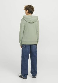 Grön bomullshuvtröja med en stor huva, ribbade ärmslut och nederkant. Bärs med lösa blå denim cargo byxor och svarta sandaler.