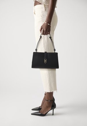 Sac à main en cuir noir au design structuré, avec des accents de ferrures dorées, et des bretelles ajustables. Porté avec un pantalon court crème et des talons noirs.
