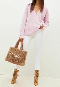 Suéter de pico rosa claro, jeans skinny blancos, botas de tacón con cordones color cuero claro y un bolso de hombro marrón de peluche con el logo "LIU JO" en beige claro.