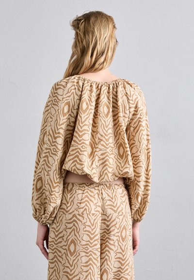 Beige gemusterte Bluse mit weit geschnittenen Ärmeln, die ein abstraktes Design in dunklerem Beige aufweist. Elastischer Ausschnitt und verkürzte Silhouette.