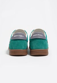 Zapatillas de ante verde con suela marrón, que cuentan con un detalle gris en el talón con el texto "BIMBA Y LOLA" en blanco.