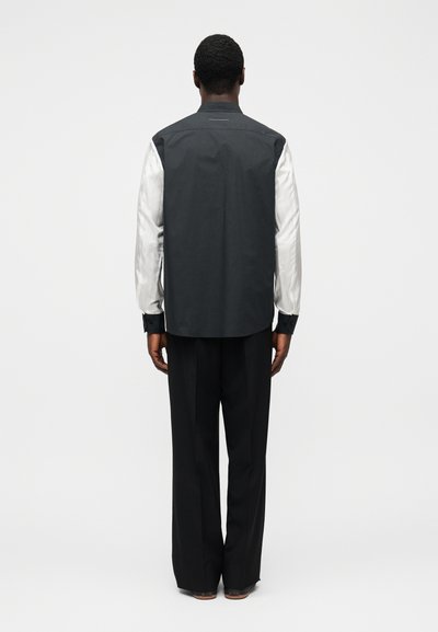 Černobílá bunda s dlouhými rukávy, vysokým límcem a hladkou texturou, doplněná volnými černými kalhotami.