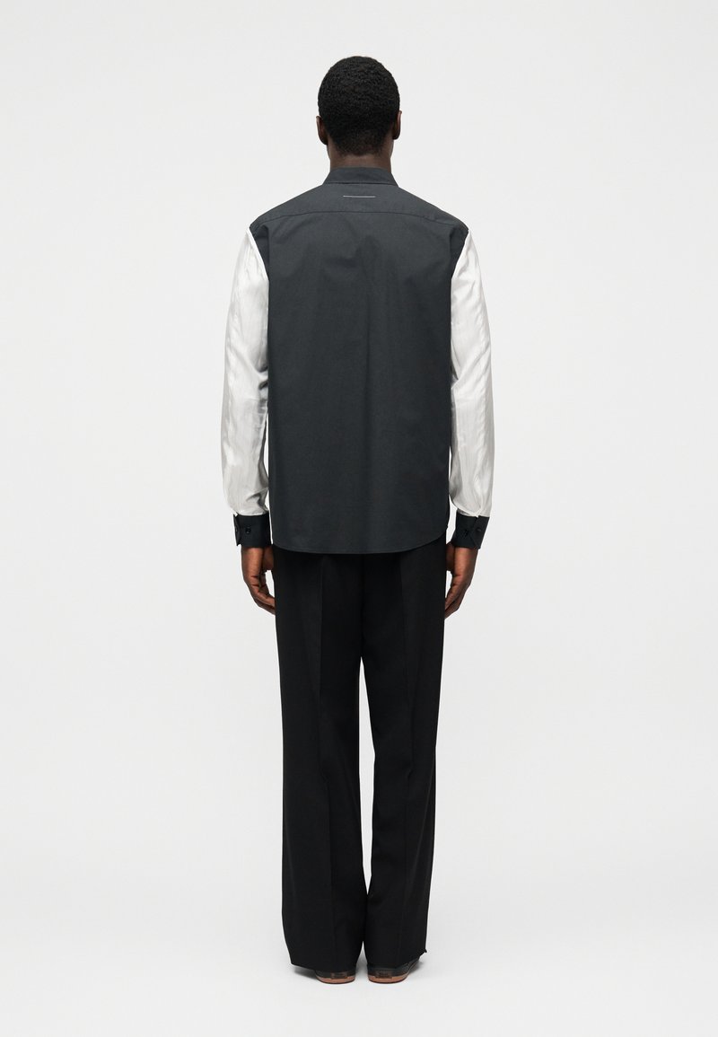 Svartvit jacka med långa ärmar, hög krage och slät textur, kombinerad med löst sittande svarta byxor.