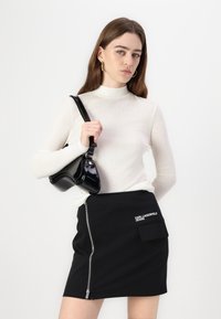 Top bianco a maniche lunghe, aderente. Gonna nera con cerniera laterale e tasca applicata, con il marchio "Karl Lagerfeld Jeans". Borsa nera in vernice.