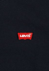 Mustast kangast, millel on väike punase ja valge Levi's logoga tikitud plaastriga, iseloomuliku kaardus kujuga ja tikitud tekstiga.