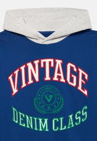 Niebieska bluza z szarym kapturem z wyhaftowanym napisem "VINTAGE" w białym i czerwonym oraz "DENIM CLASS" w zielonym, a także dekoracyjnym okrągłym logo.
