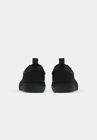 Sneaker nere con tomaie in tessuto liscio, suole in gomma piatte e linguette sul tallone; design minimalista senza motivi o accenti visibili.