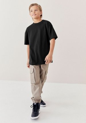 Schwarzes Baumwoll-T-Shirt mit kurzen Ärmeln, kombiniert mit beigefarbenen Cargo-Hosen mit Seitentaschen und elastischen Bündchen, getragen mit schwarzen Sneakers.