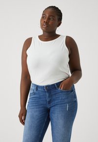 White ribbed tank top paired with blue denim jeans. The jeans feature a front pocket and slight fading. Simple design with a fitted silhouette.