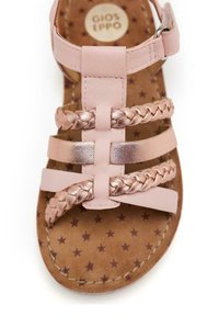 Sandalia rosa con acentos trenzados metálicos, que cuenta con múltiples tiras ajustables. El interior tiene un diseño de estrella sobre una base marrón.