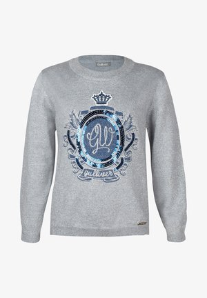 Pull argent à col rond, arborant un motif de blason en sequins bleus et noirs. Il a des manches longues et une texture légèrement scintillante.