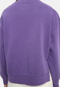 Fioletowa bluza wykonana z miękkiej bawełny. Charakteryzuje się luźnym krojem, okrągłym dekoltem i ściągaczami na rękawach. Gładka faktura z minimalną ilością szwów i bez zdobień.