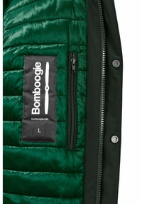 Giubbotto imbottito verde scuro con finitura testurizzata, dotato di un'etichetta nera con logo bianco, tasca laterale con zip e dettagli con chiusura a pressione.