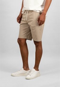 Beige shorts dengan pinggang elastis dan tali serut. Dipadukan dengan sepatu sneakers putih, memiliki desain rendah dan tali sepatu yang sederhana.