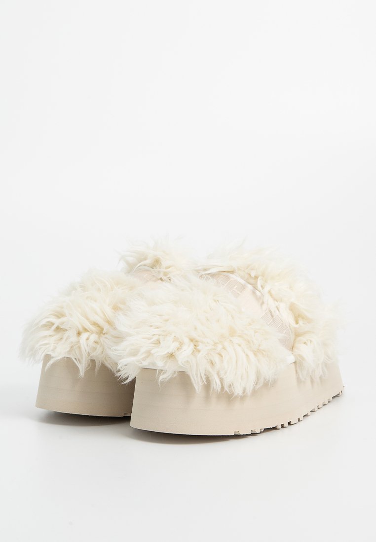 Puszyste białe klapki na platformie z teksturowanym, sztucznym futrem u góry i grubą, beżową gumową podeszwą. Minimalistyczny design bez widocznych elementów metalowych.
