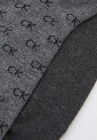 Calzini grigi con un sottile motivo ripetuto del logo "CK", caratterizzati da una texture liscia e da una base grigio scuro nelle zone del tallone e della punta.