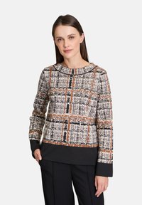 Knit sweater featuring a textured, multicolored plaid pattern in shades of brown, black, and cream, with long sleeves and a crew neckline.