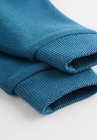 Poignets de sweat-shirt en coton bleu sarcelle avec texture côtelée. Fini lisse et bords roulés, affichant une couleur uniforme et des coutures régulières.